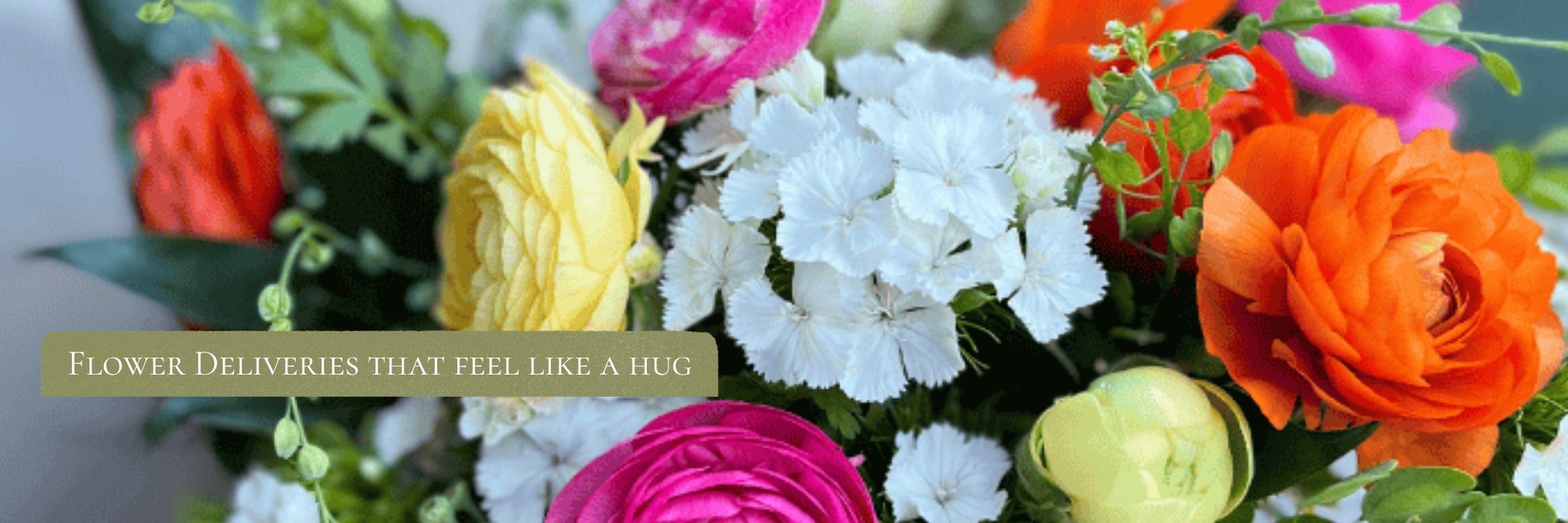 Bright bouquet of pink, orange, yellow ranunculus and white dianthus with text reading Flowers that feel like a hug